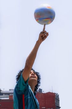 A man skillfully spinning a colorful ball on his finger against a sunny sky.