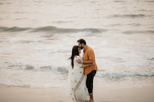 A Man Kissing a Woman on the Forehead while Standing on the Shore