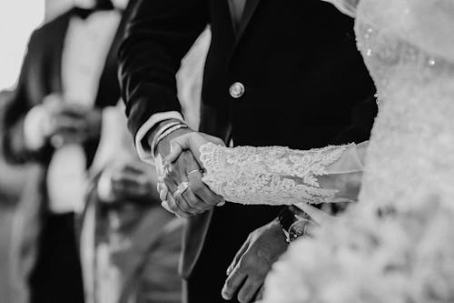 Grayscale Photo of Man and Woman Holding Hands During Their Wedding 