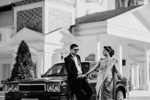 Man in Tuxedo Leaning against a Car and Holding Womans Hand 