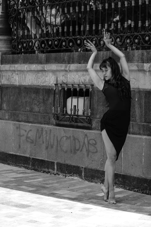 Grayscale Photo of a Woman in Black Dress Dancing on Sidewalk