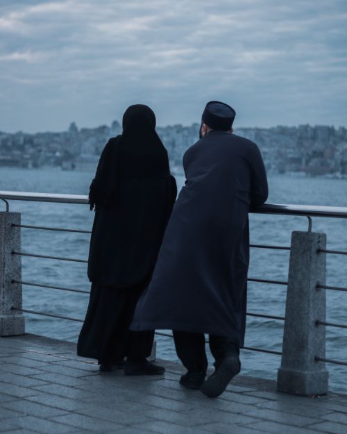 Free A couple in traditional attire enjoys a serene moment on a pier with a distant cityscape view under a twilight sky. Stock Photo