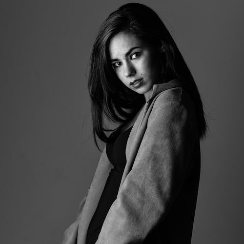 A Grayscale Photo of a Woman Wearing a Coat while Looking Over Shoulder
