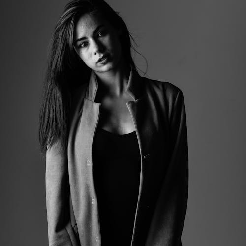 A Grayscale Photo of a Woman Wearing a Coat while Looking with a Serious Face