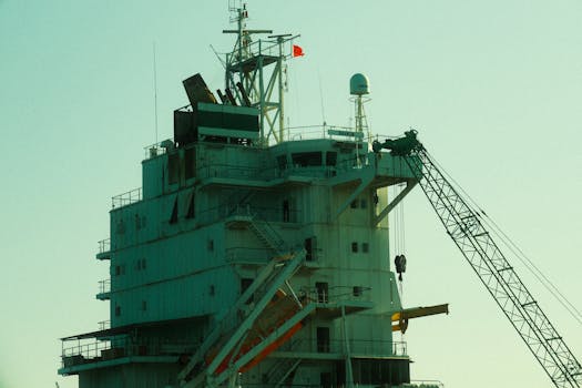 Close-up of an industrial ship's structure and crane against a sunset backdrop.