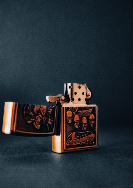 Close-up of an open vintage metal lighter with detailed engraving, against a dark background.