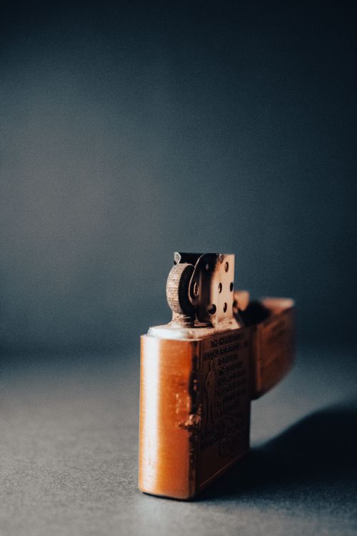 Free A detailed vertical shot of a vintage metal lighter on a gray surface with artistic lighting. Stock Photo