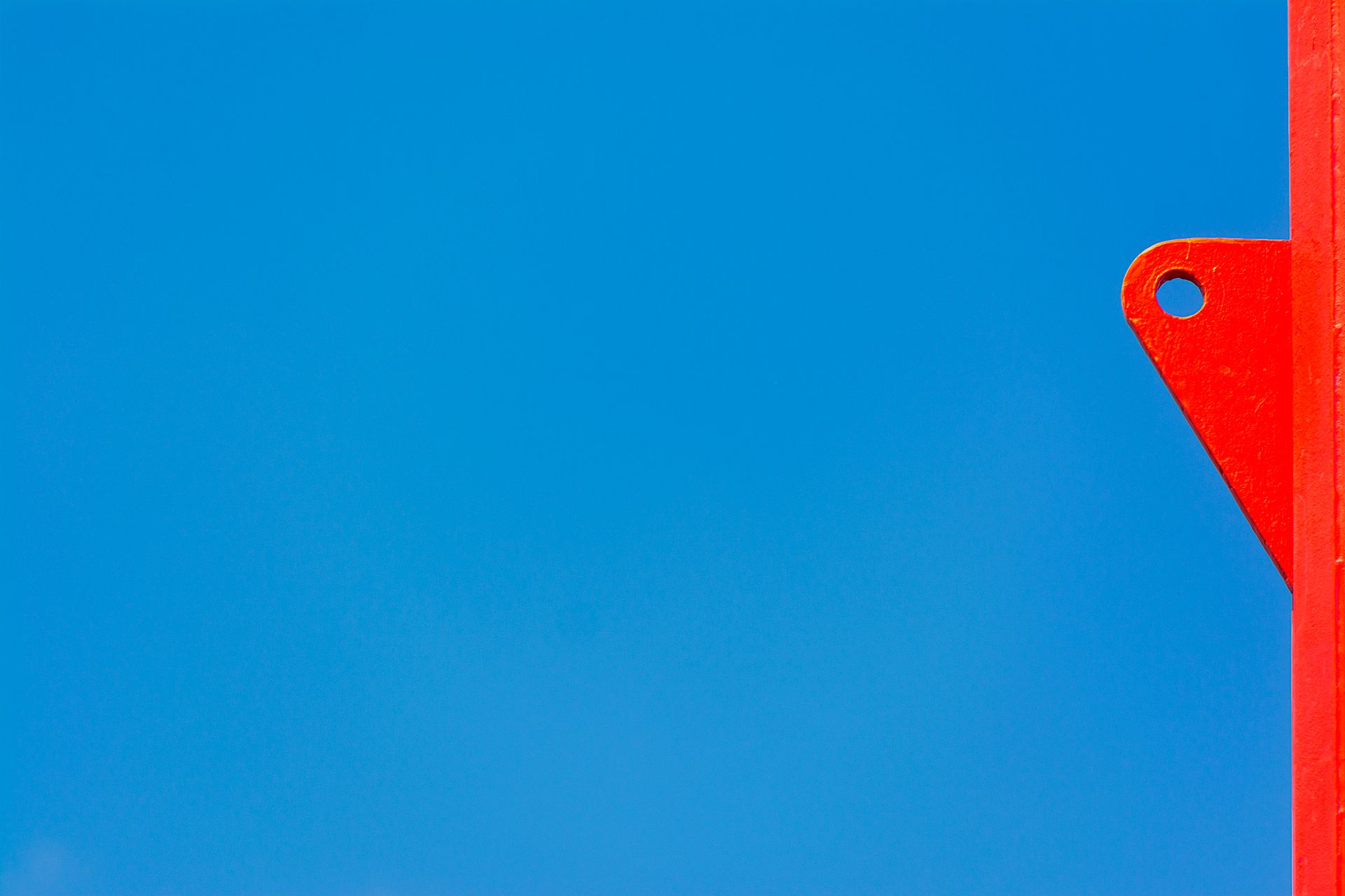 A bright red metal post against a clear blue sky, creating a vibrant minimalist composition.
