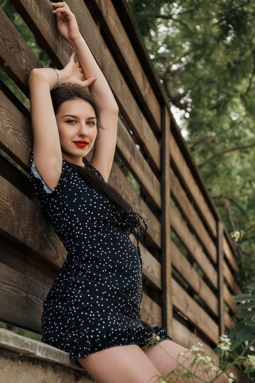 Free Beautiful woman in a polka dot dress posing elegantly by a wooden fence outdoors. Stock Photo