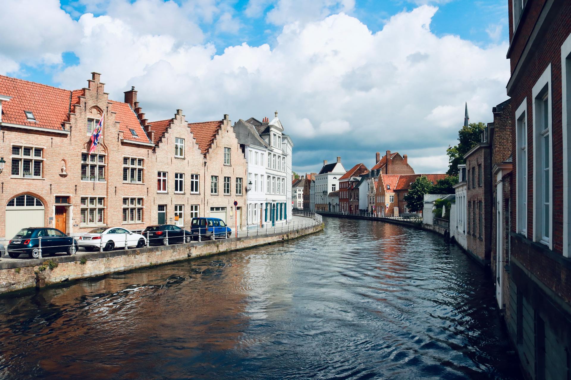 Scenic view of Bruges canal lined with historic gabled buildings under a blue sky.