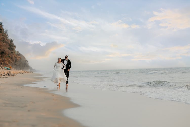 A Bride And Groom Running On The Beach