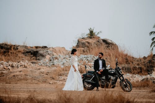 A Man Sitting on the Motorcycle While Looking the Woman in Wedding Dress