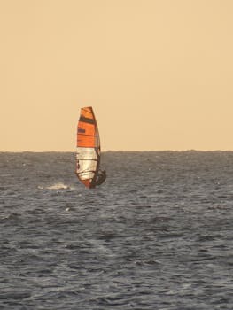 A solo windsurfer enjoys the calm waters under a golden sunset sky, capturing a moment of adventure and tranquility.
