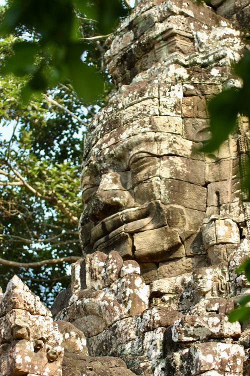 Free Close-up of a smiling stone face at Angkor Thom temple, surrounded by greenery, in Cambodia. Stock Photo