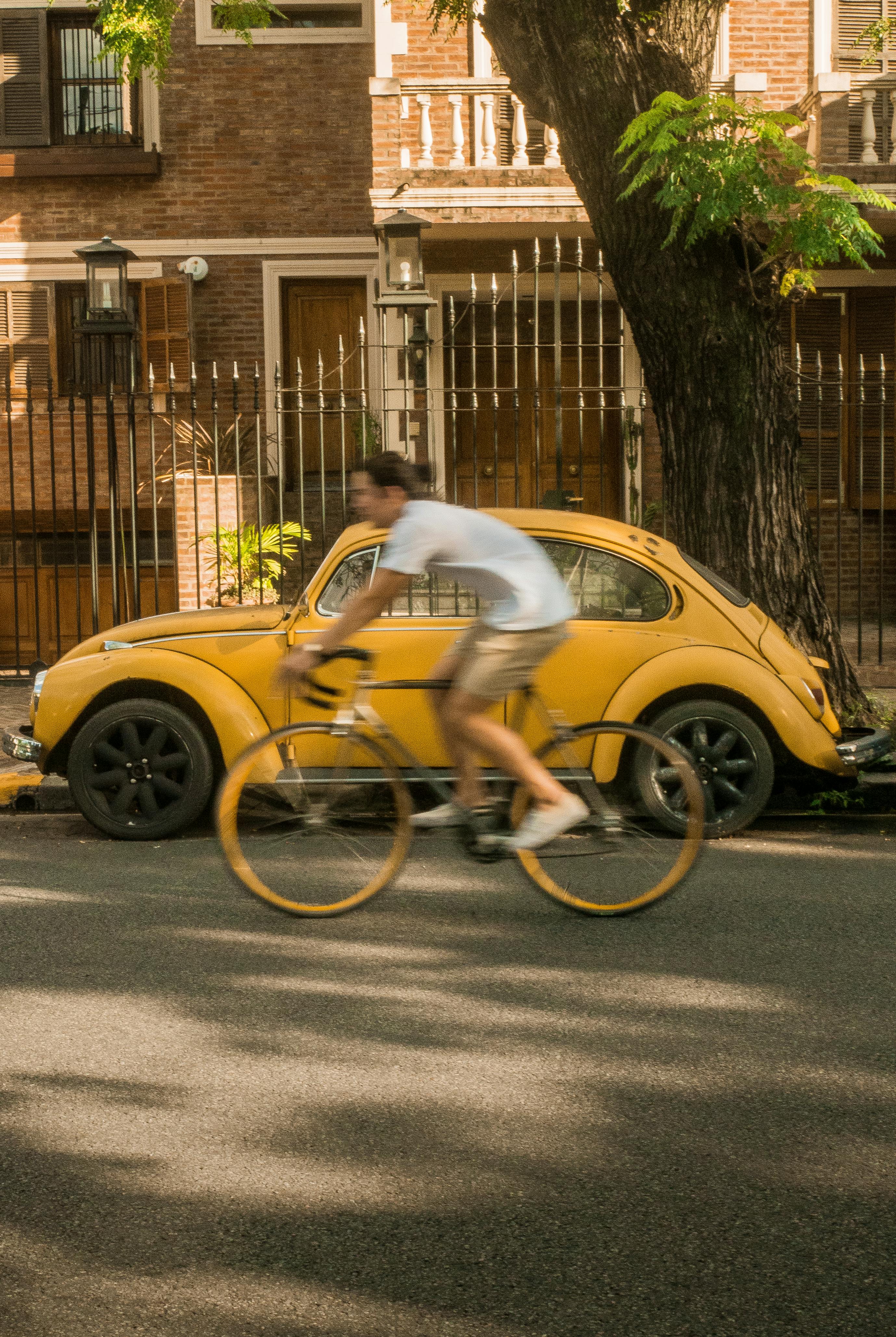 A cyclist rides past a parked vintage yellow car on a sunny day in Buenos Aires, Argentina.