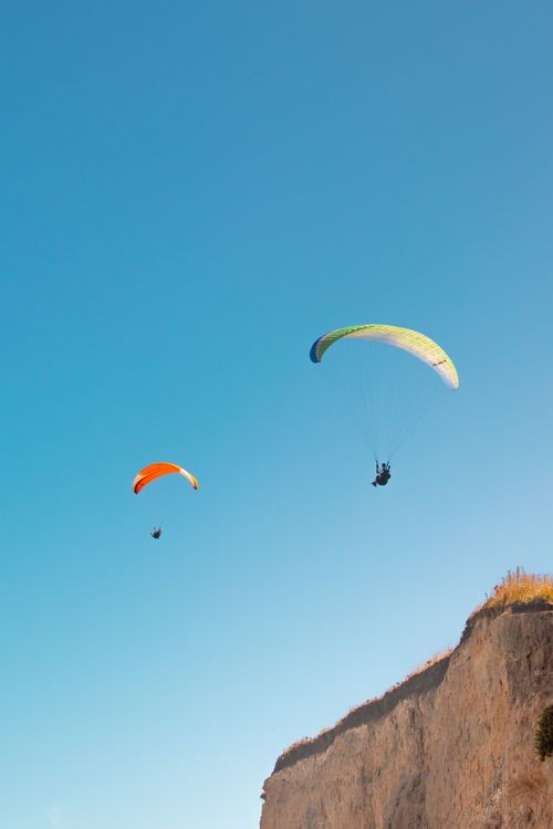 Free Two paragliders soar above cliffs in Mar del Plata, Argentina, under a clear blue sky. Stock Photo