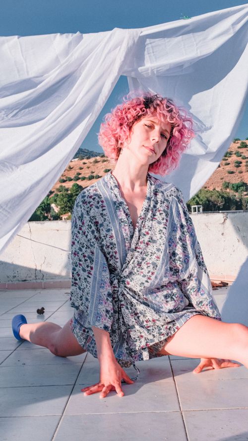 Free A woman in a floral robe performs splits on a tiled outdoor terrace under blue skies. Stock Photo
