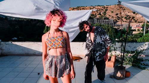 Free Young couple in vibrant patterned outfits on a sunny rooftop with a picturesque backdrop. Stock Photo