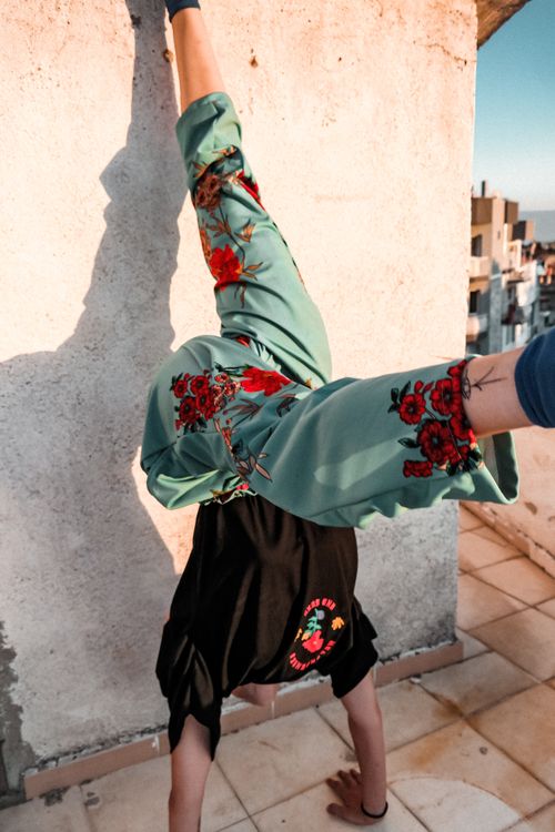 Free A person performs a handstand against a wall in an urban setting, showcasing floral embroidered pants. Stock Photo