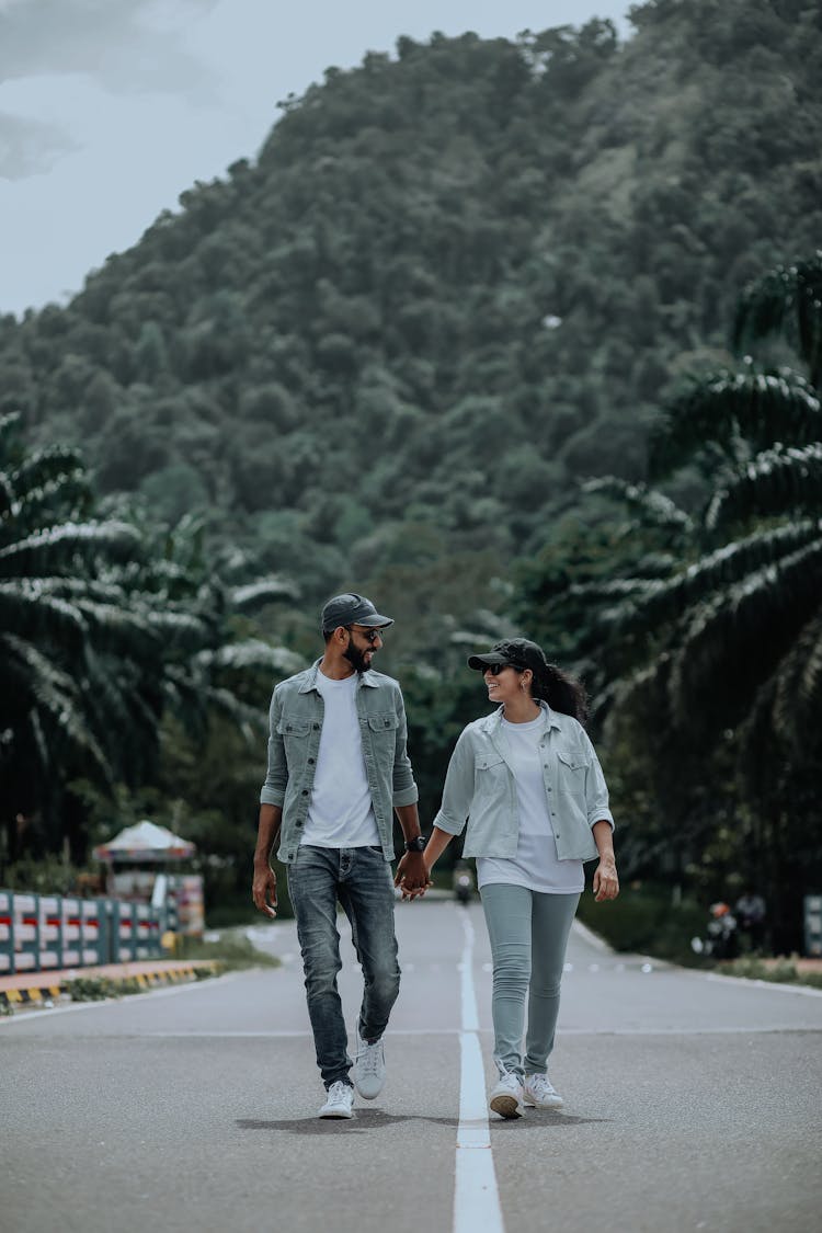 A Couple Walking On The Road While Holding Each Others Hand