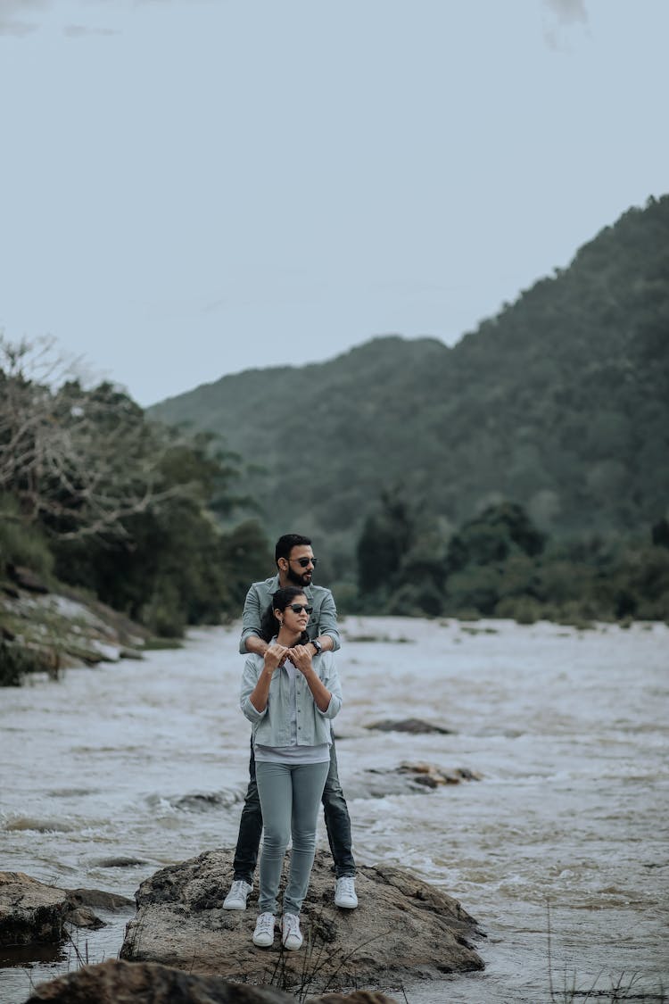 A Couple Standing On Big Rock Near The Lake 