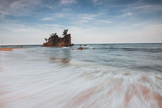 A tranquil beach scene with a rock formation and calm ocean captured using long exposure technique.
