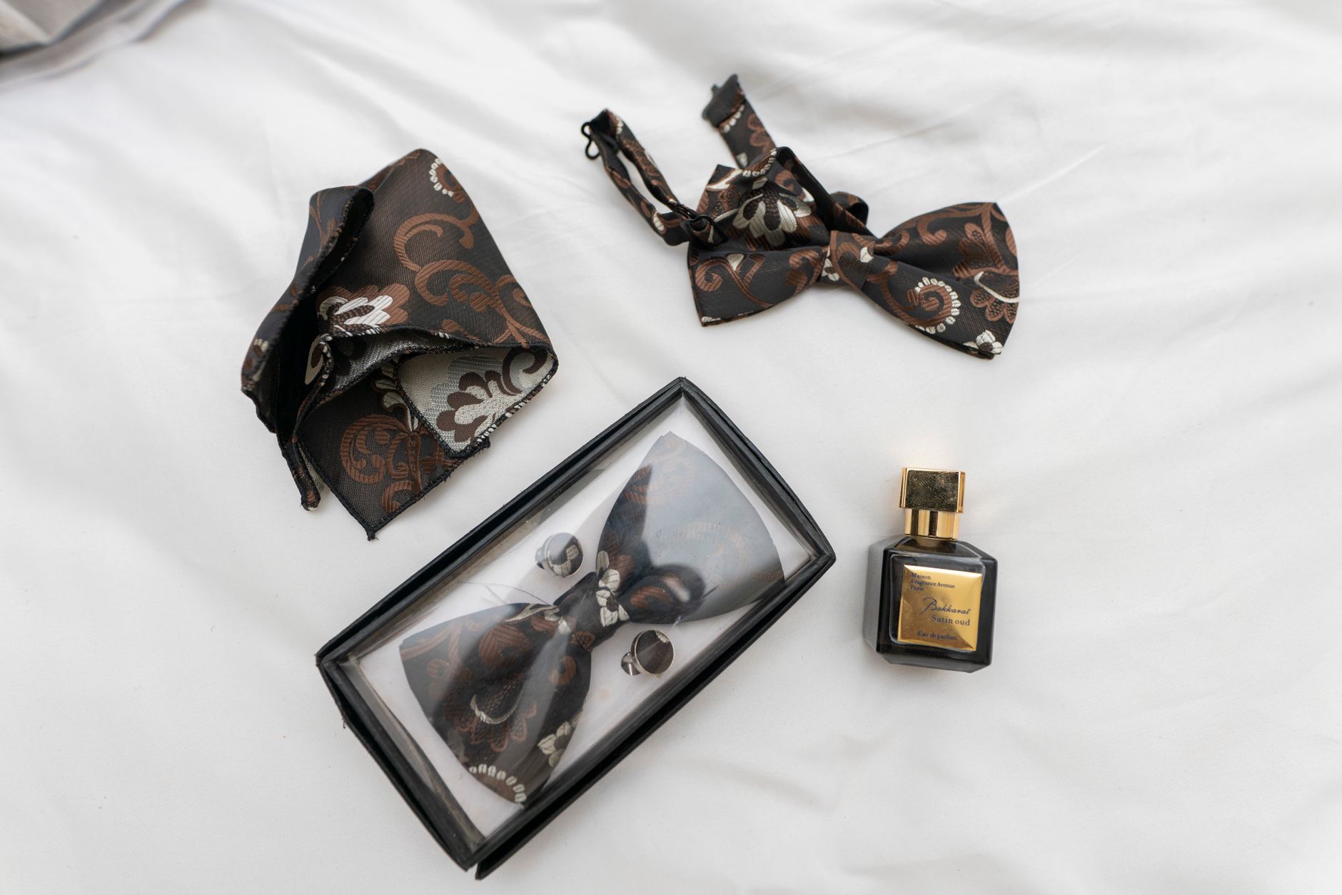 Stylish bow tie and perfume set on white fabric, capturing elegance and sophistication.