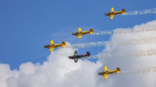 Free Five vintage planes performing an aerobatic stunt with contrails against a clear blue sky. Stock Photo