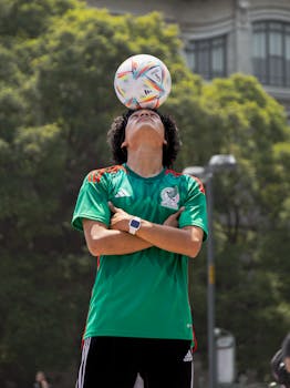 A young man balances a soccer ball on his head in an outdoor setting in Mexico City, showing skill and concentration.