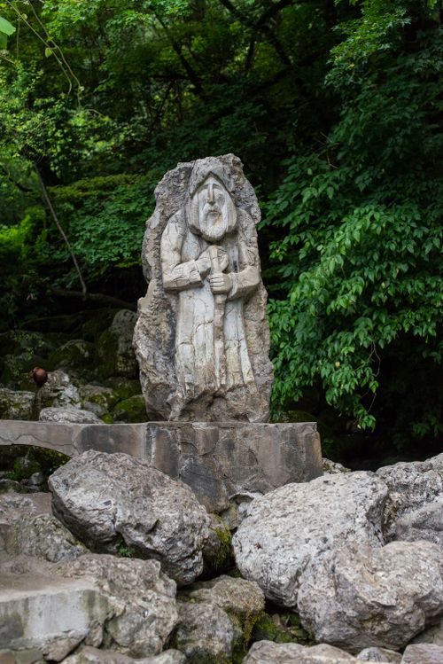 Free A carved stone sculpture of a male figure situated in a lush, forested area. Stock Photo