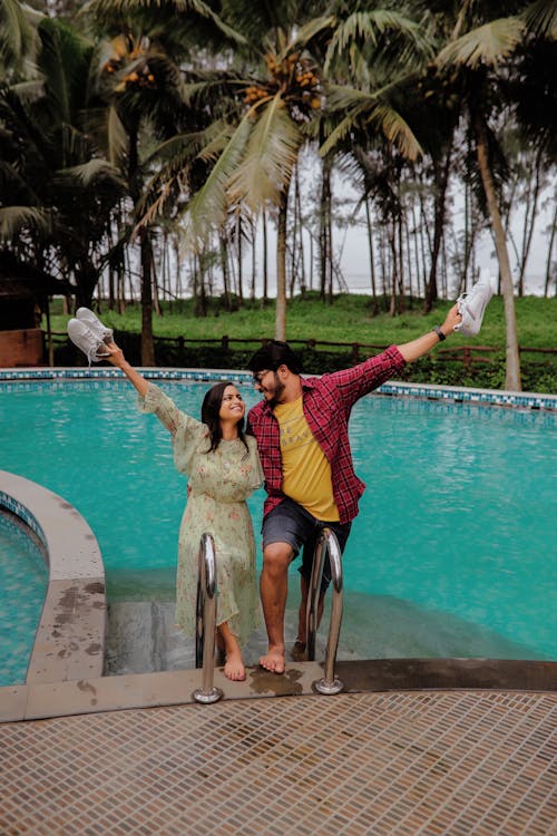 A Sweet Couple Holding White Sneakers while Standing on the Poolside