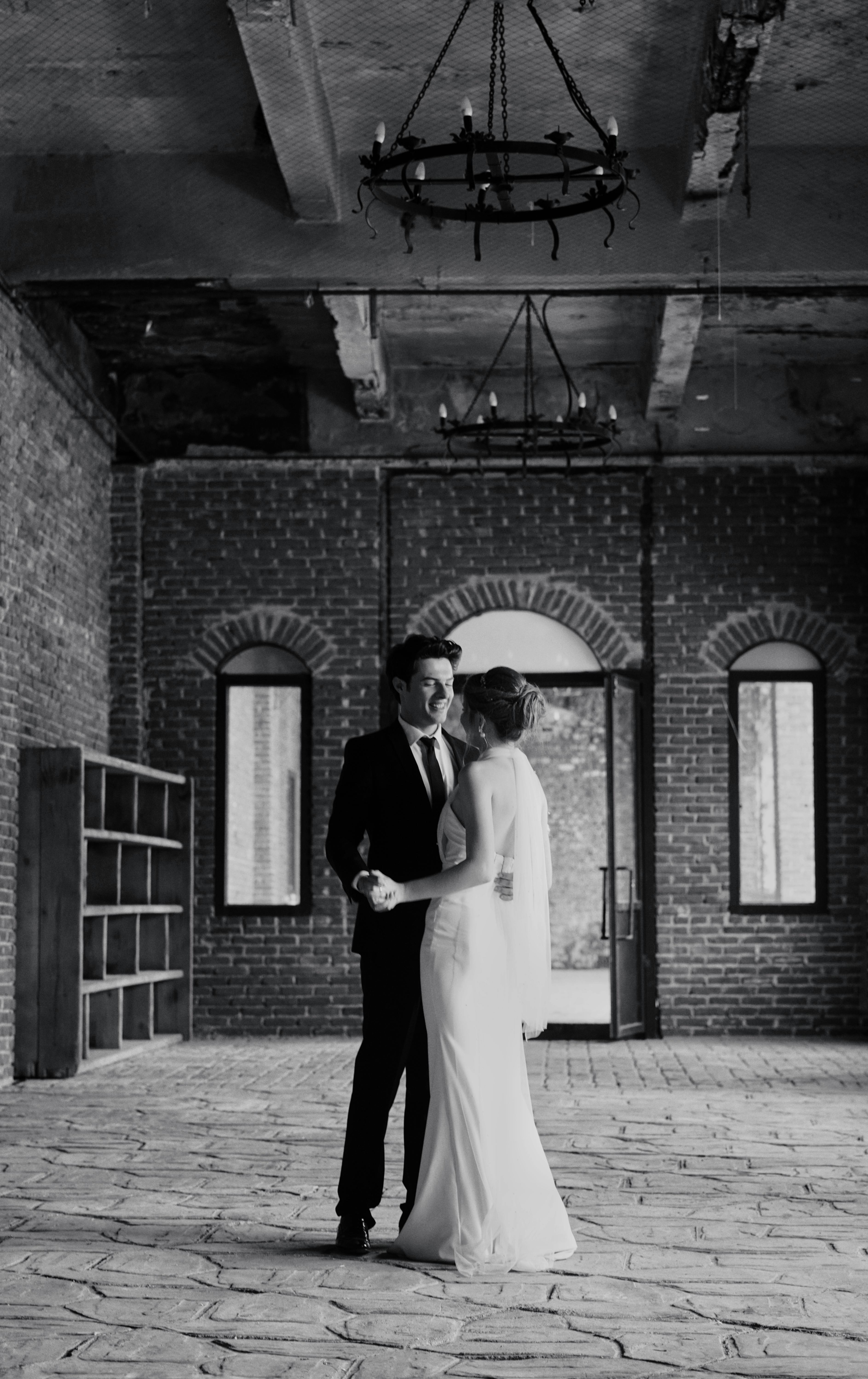 Black-and-white photo of a couple at an industrial wedding venue, embracing romantically.