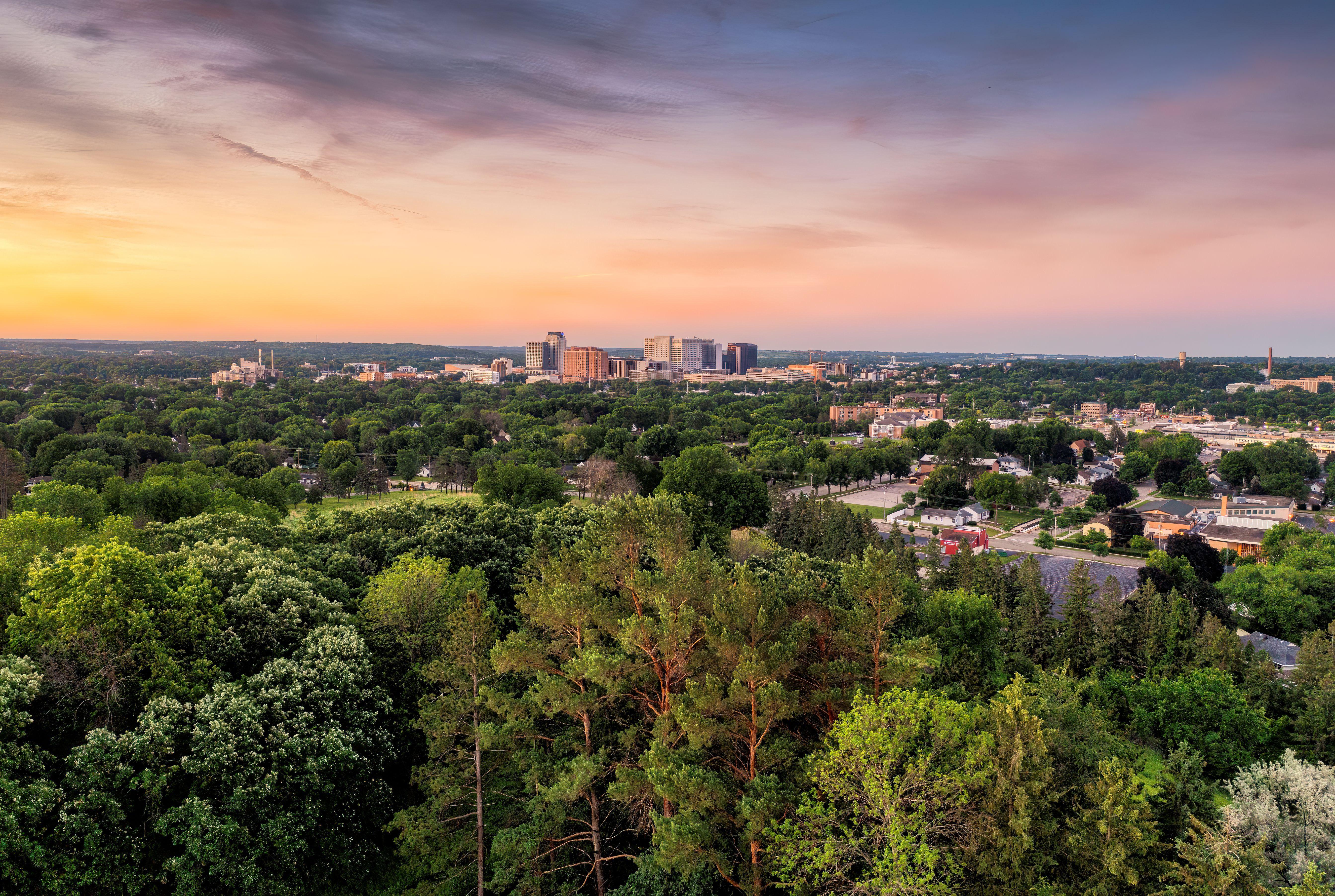 Breathtaking aerial view of Rochester, MN skyline surrounded by lush greenery at sunset.