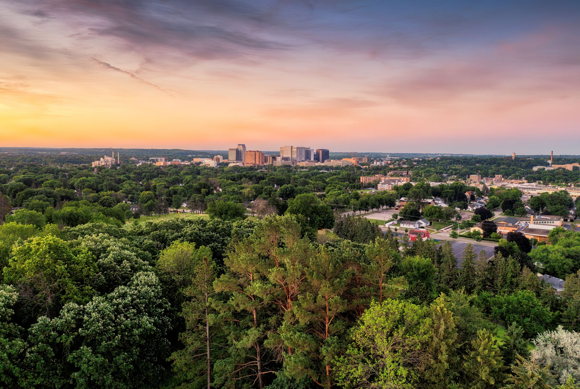 Breathtaking aerial view of Rochester, MN skyline surrounded by lush greenery at sunset.