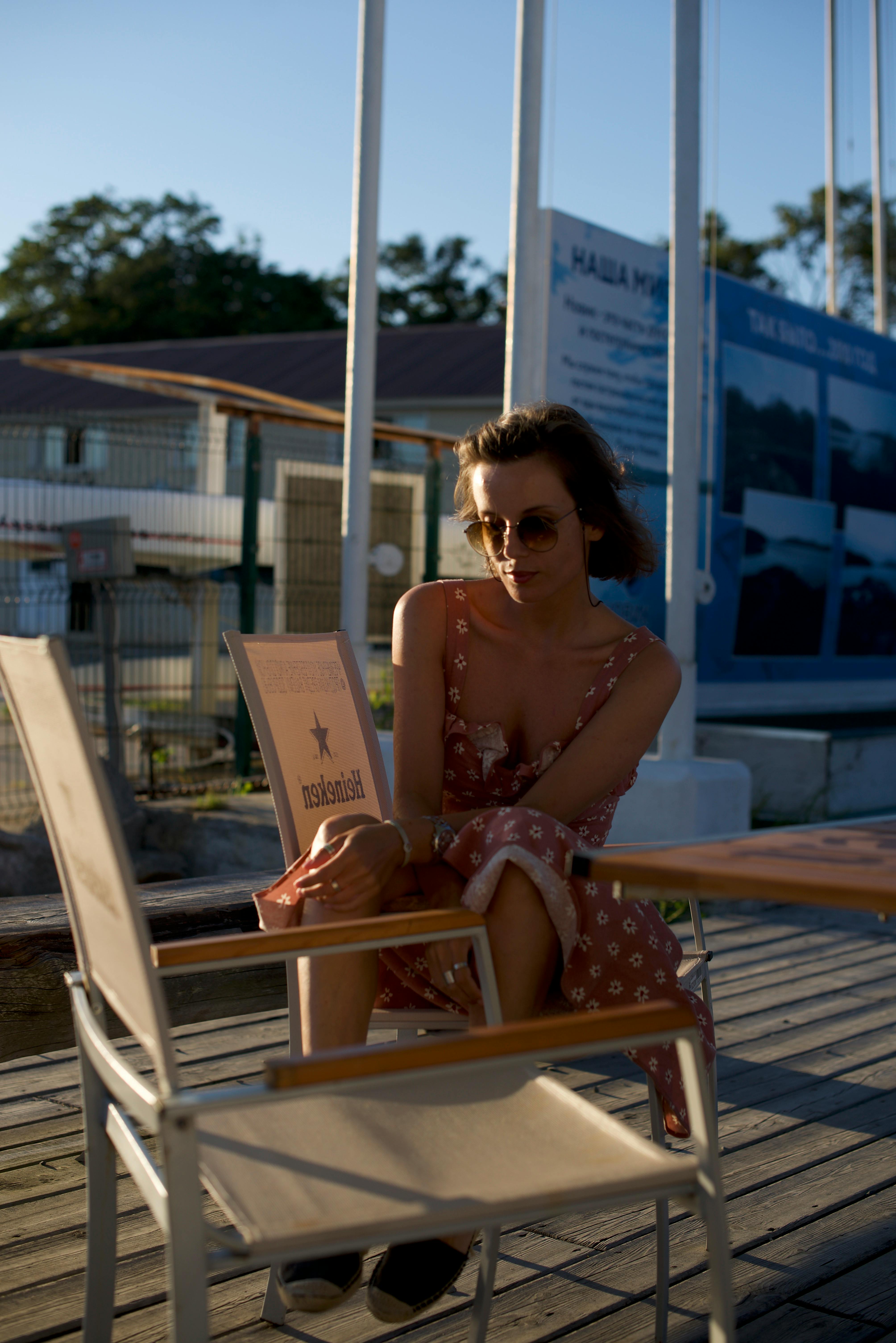 Woman in pink dress and sunglasses sitting outdoors with a relaxed demeanor.