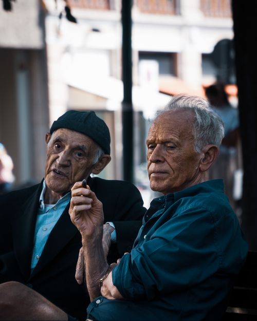 Free Two elderly men engaged in conversation on a park bench, captured in a candid moment on a sunny day. Stock Photo