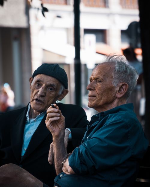 Free Two senior men sit together outdoors, talking and smoking in a lively discussion. Stock Photo