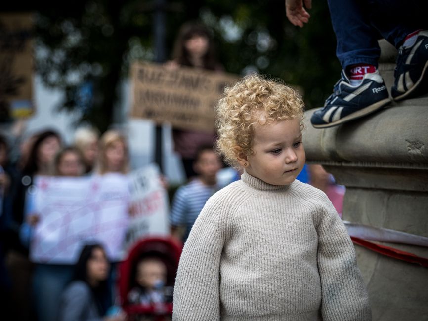 A young child observing a peaceful protest with people holding banners outdoors.