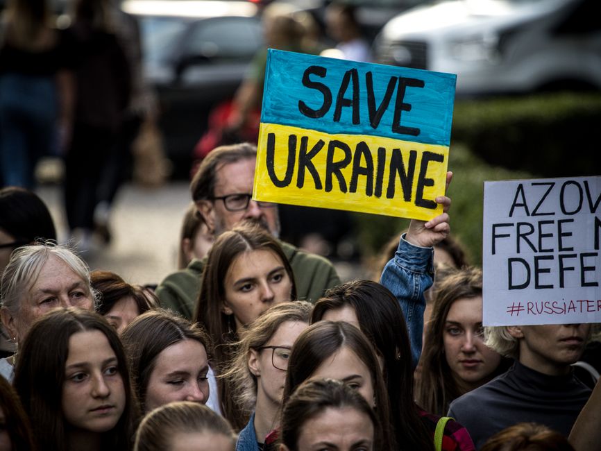 A diverse crowd holds signs supporting Ukraine during a protest rally.