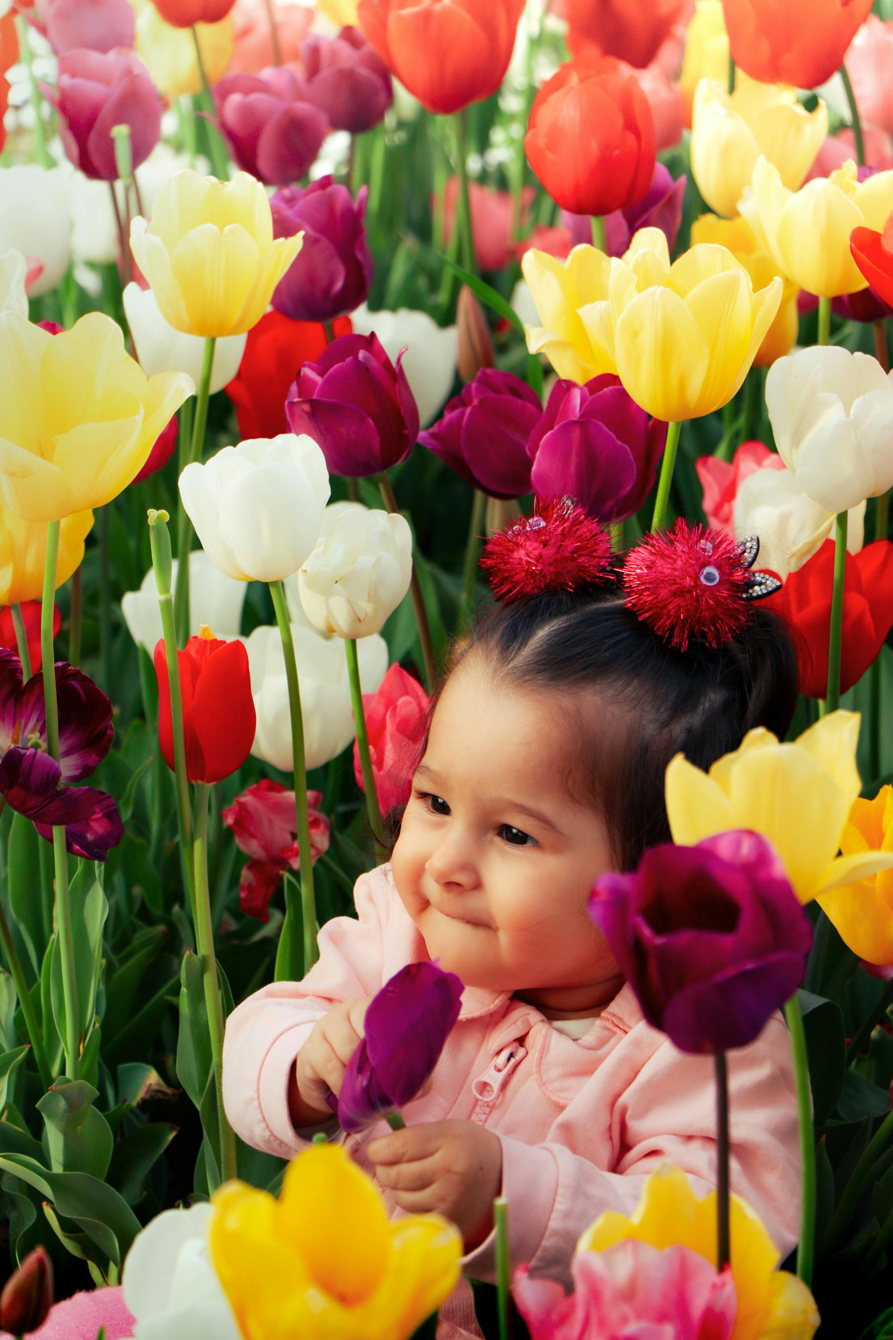 Adorable baby sitting among colorful tulips in a garden in Istanbul, Türkiye.