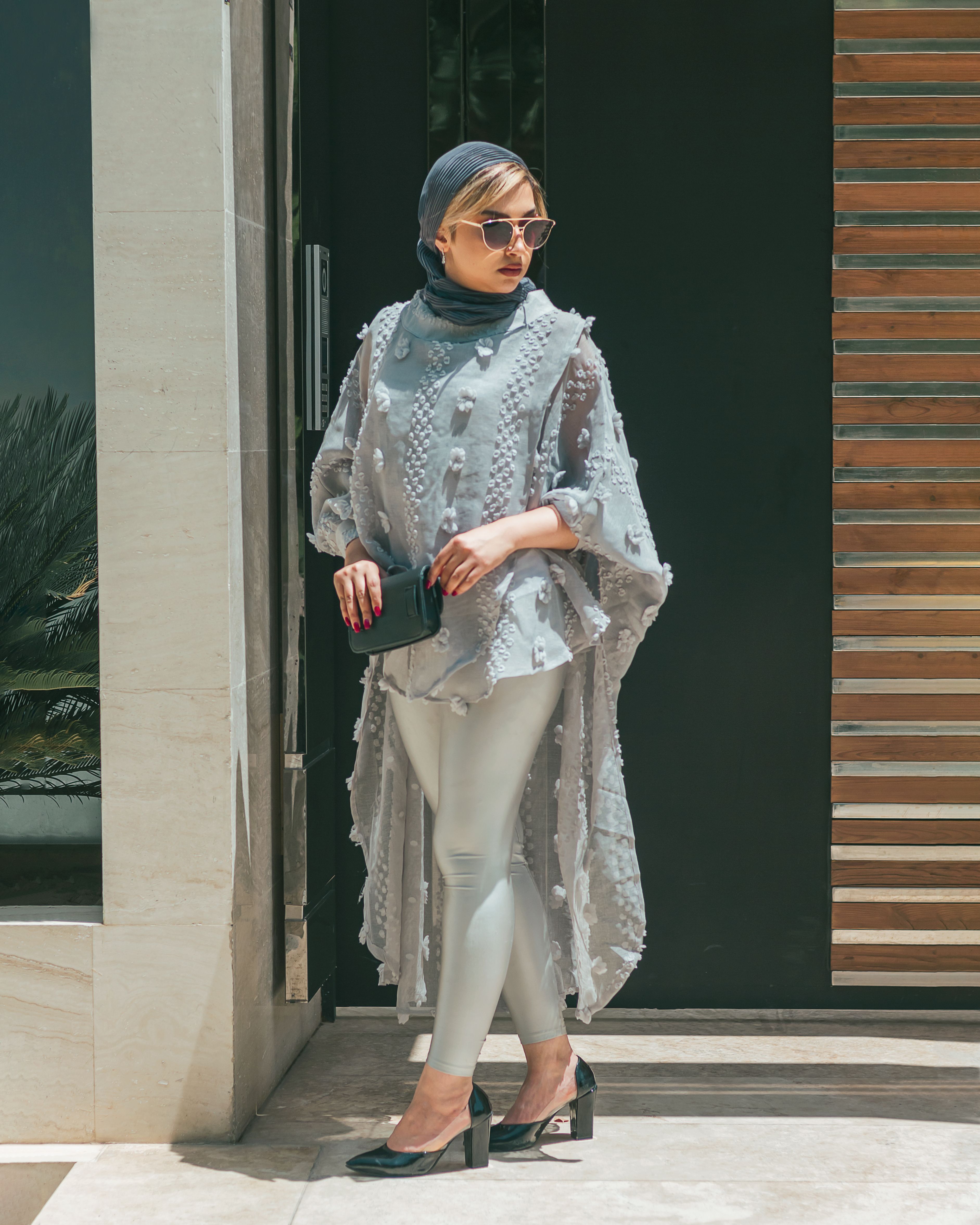 Fashionable woman wearing a stylish outfit with sunglasses, standing outdoors.
