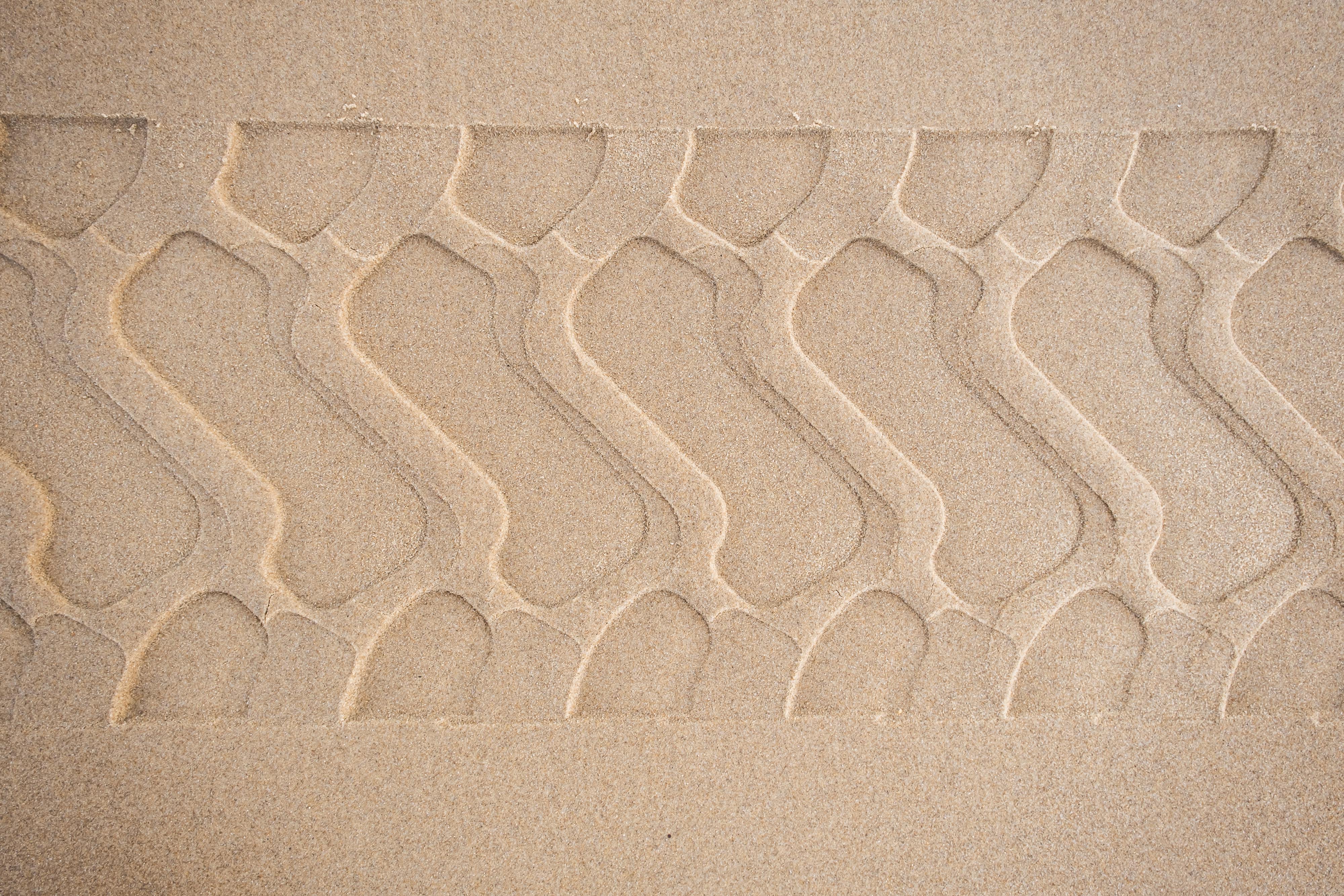 Close-up of intricate tire track pattern on desert sand, showing texture and detail.