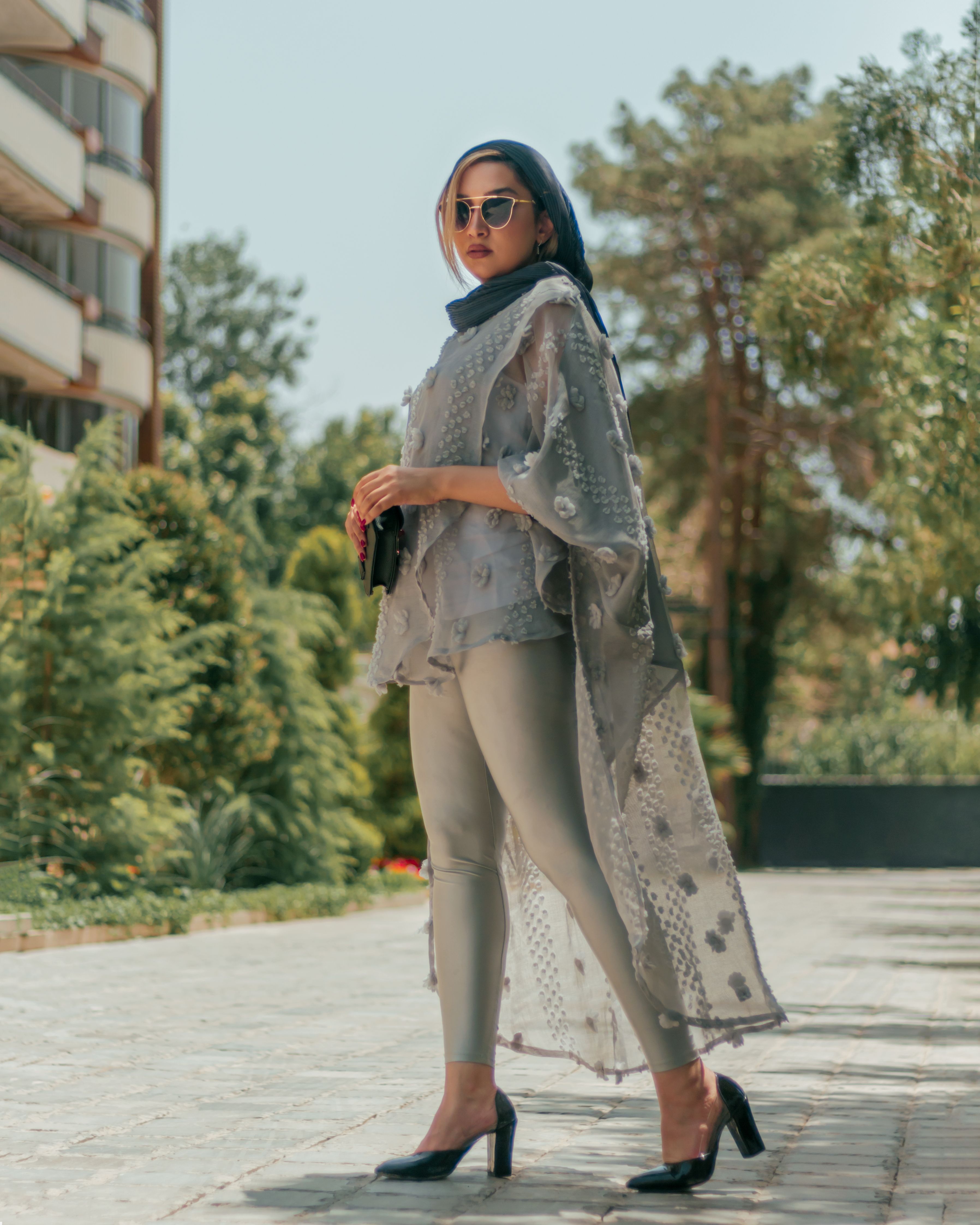 Stylish woman wearing a headscarf and sunglasses posing confidently in modern street fashion.