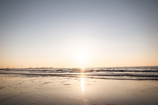 Calm beach scene at sunrise with gentle waves reflecting sunlight.
