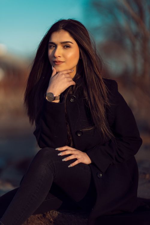Free Portrait of a smiling woman in a black coat sitting outdoors with her hand on her chin. Stock Photo