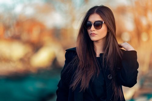 Free Fashionable woman wearing sunglasses and black coat, posing outdoors in natural light. Stock Photo
