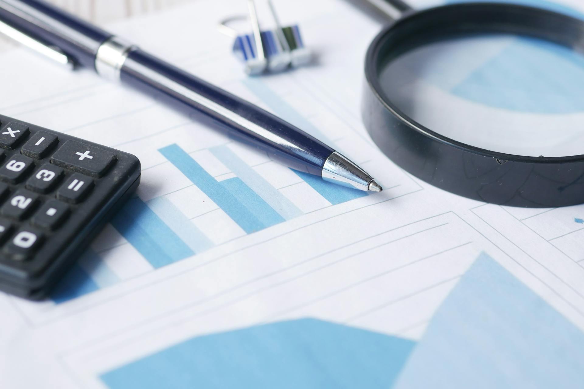 Close-up of calculator, pen, and magnifying glass on financial documents.