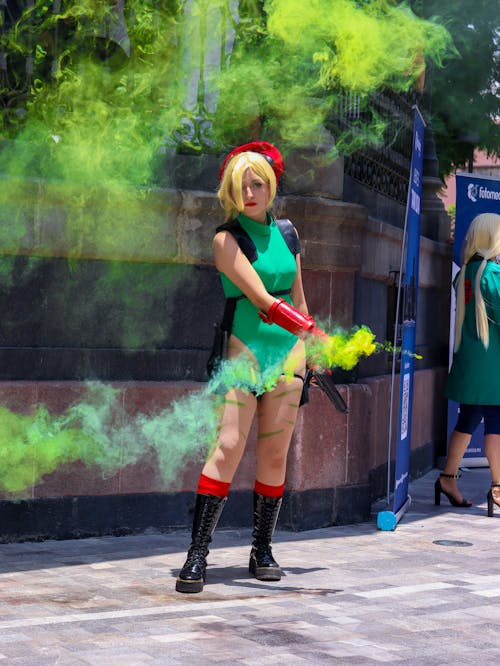 A Woman in Green Bodysuit and Black Boots Standing on the Street while Holding a Smoke Bomb