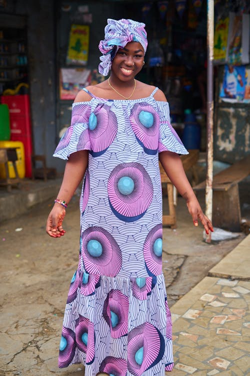 A Woman in Printed Dress Smiling while Standing on the Street