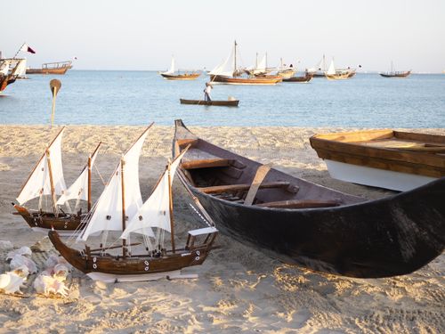 Free Traditional fishing boats and miniature dhows on a sandy beach in Doha, Qatar, under a bright sky. Stock Photo